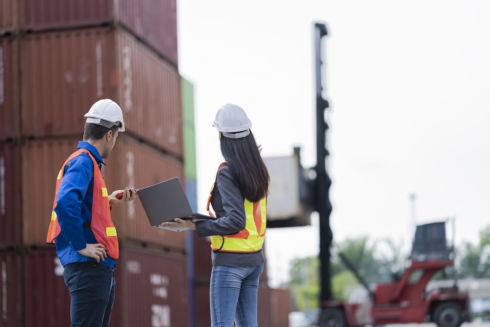 Two logistics workers man and woman discuss operations at a busy shipping container yard. successful coordination in freight, transportation, and supply chain operations